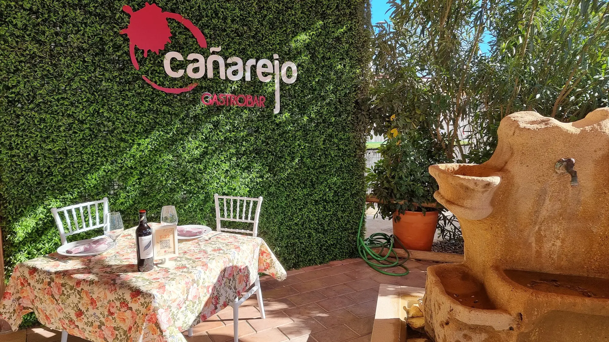 Terraza de Cañarejo: mesa junto a la pared vegetal con el logo y la fuente de piedra